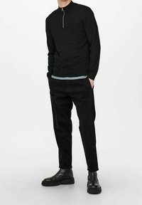 Zwarte lange mouwen pullover met een hoge kraag en een rits aan de voorkant, gecombineerd met zwarte slim-fit broek en zwarte enkellaarzen. Soepele textuur.