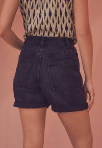 Pantalones cortos de mezclilla negra con cintura alta, dobladillos enrollados y dos bolsillos traseros. Diseñados con una textura suave y un ajuste casual.