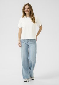 Hvid t-shirt med kortærmer og sort kant, parret med lysblå bredbenede jeans. Sættet afsluttes med grå og hvide sneakers.