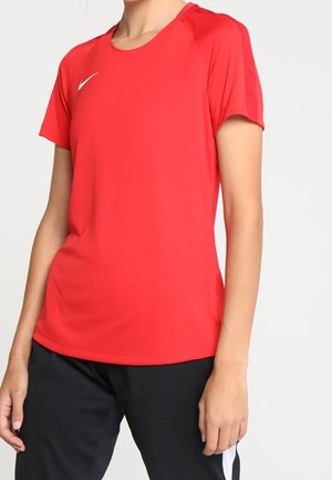 Kvinde iført en rød kortærmet sportstrøje med et hvidt Nike-logo, kombineret med sorte bukser med en hvid stribe.