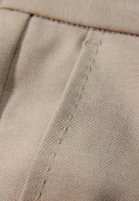 Close-up van beige stof met gedetailleerd stiksel en een gestructureerd weefpatroon op gevouwen materiaal.