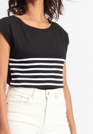 Czarny top z krótkim rękawem z poziomymi białymi paskami na środku, połączony z białymi, wysokim stanem spodniami. Miękki bawełniany materiał.