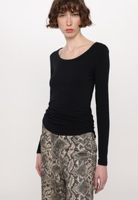 Zwarte langemouwen top met een ronde hals en verzamelde details, gecombineerd met een broek met een beige en bruine slangenprint.