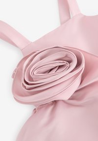 Rosa klänning med satinliknande textur och en rullad tygdetalj vid midjan samt tunna axelremmar. Slätt, mjukt material med en subtil lyster.