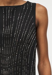 Μαύρο φόρεμα χωρίς μανίκια, διακοσμημένο με κάθετες και καμπυλωτές γραμμές από μικρά ασημένια ορθογώνια και στρογγυλά τρουκ.