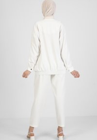 Witte, losvallende jas met ritssluiting, een tailleband en manchetten met knopen, gecombineerd met bijpassende taps toelopende broek, minimale textuur en zonder patronen.