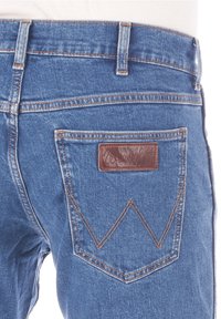 Modré džíny z denimu s hnědou koženou nášivkou a charakteristickým cik-cak prošitím na zadní kapse. Klasický design s pěti kapsami, střední pas.