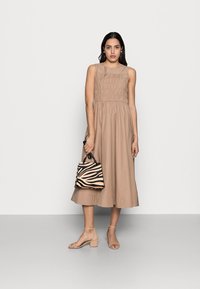 Beiges ärmelloses Kleid mit gerafftem Oberteil, fließendem Rock, kombiniert mit einer kleinen schwarz-beigen Tasche im Zebramuster und hautfarbenen Blockabsatzsandalen.