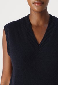Maglione senza maniche blu navy con scollatura a V, realizzato in tessuto morbido e testurizzato. I dettagli a coste sul colletto aumentano l'interesse visivo.