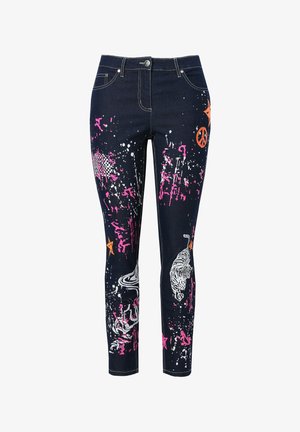 Jeans in denim scuro caratterizzati da vivaci macchie di vernice rosa e arancione, design grafici di una tigre, simbolo della pace e stelle.