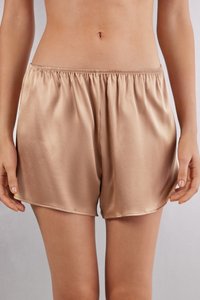 Pantalones cortos de satén en un suave color beige con cintura elástica, con una textura lisa y un ajuste holgado.