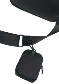 Czarna torebka crossbody z teksturowanym nylonowym korpusem, posiadająca odpinaną małą saszetkę przypinaną metalowym klipsem oraz regulowany pasek.