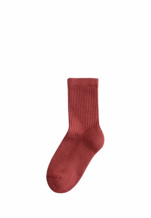 Calza a coste color ruggine realizzata in tessuto morbido. Lunghezza alla caviglia con un design classico, caratterizzata da una superficie liscia e un tallone rinforzato.