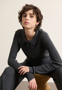 Top grigio a coste con colletto e pattina con bottoni, abbinato a pantaloni coordinati sempre a coste. Morbida texture, vestibilità slim e maniche lunghe.