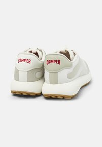 Sneaker bianche con accenti beige e scritta "CAMPER" in rosso sul tallone, che mostrano un design moderno e sportivo.