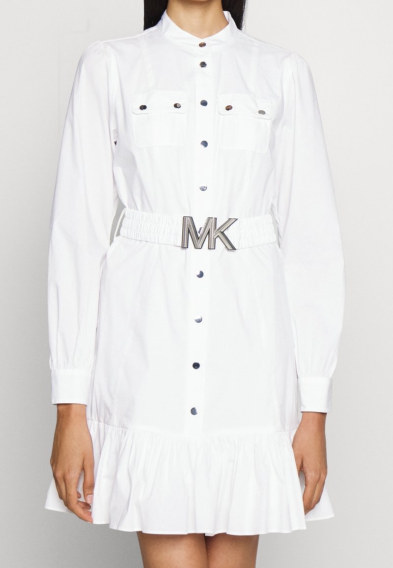 Abito bianco in cotone misto, con colletto, maniche lunghe a sbuffo, chiusura frontale con bottoni, due tasche sul petto e orlo arricciato. Include una vita aderente con una cintura con logo MK.