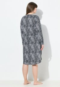 Pitkähihainen mekko musta-valkoisella leopardikuviolla, löysällä istuvuudella, pyöreällä kaula-aukolla ja sivuaukkoja helmassa liikkumisen helpottamiseksi.