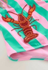 Wieloryb wyhaftowany na różowo-zielonym paskowanym materiale, z koralikowymi detalami, gładką teksturą i dopasowanym krojem.