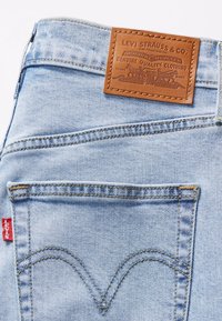 Světle modré džínové kalhoty s koženou značkovou nášivkou, dvěma zadními kapsami a ikonickým zakřiveným prošíváním na švech kapes.