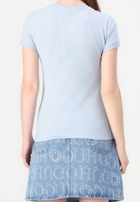Maglietta aderente azzurra con maniche corte e scollo rotondo, abbinata a una gonna di jeans blu con un motivo a logo ripetuto.