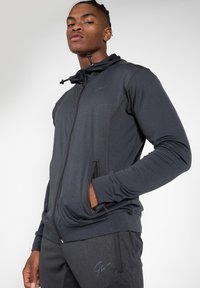 Zwarte zip-up hoodie met trekkoord en ritszakken. Gladde stof met contrasterende naden, voorzien van een klein logo op de borst.