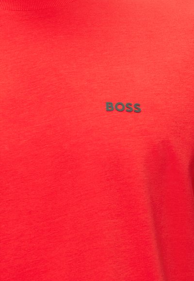 Tissu rouge avec un petit texte noir "BOSS" imprimé sur la zone haute de la poitrine d'un vêtement.
