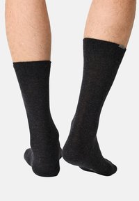 Dunkelgraue Baumwollsocken mit Rippstruktur und verstärkten Bündchen, von hinten an nackten Beinen gezeigt, mit glattem Stoff und Knöchelhöhe.