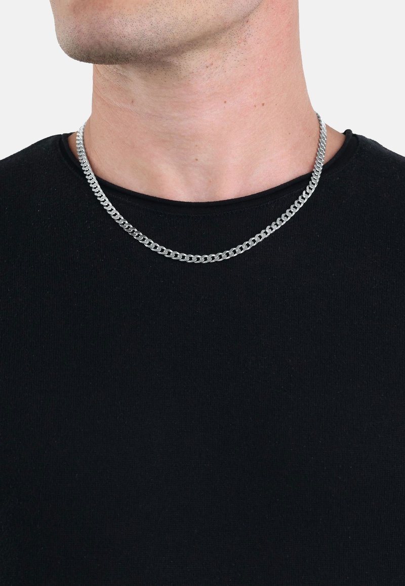 Collana in argento con maglie intrecciate, indossata su una maglietta nera a girocollo. Presenta una superficie liscia e lucida.
