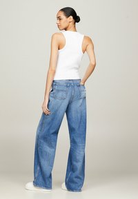 Top sin mangas blanco combinado con jeans de corte holgado en un azul claro y zapatillas blancas. Los jeans cuentan con bolsillos traseros y sutiles detalles de costura.
