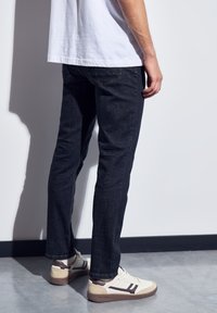 Tmavě modré džíny s rovný fit, viditelným šitím a dvěma zadními kapsami. V kombinaci s bílými teniskami s hnědými akcenty.