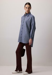 Blå ternet skjorte med lange ærmer, to brystlommer, parret med strammende brune flared bukser og hvide sko.