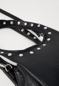 Borsa a tracolla in pelle nera testurizzata con borchie circolari in argento che decorano il bordo esterno e una tracolla removibile.