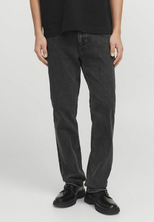 Jeans de denim negro con un corte recto, las características incluyen costuras en contraste, cinco bolsillos y una textura desgastada. Combinados con zapatos negros.