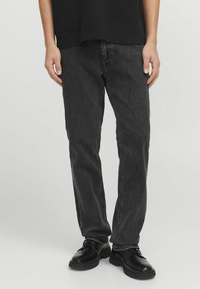 Jeans in denim nero con fit dritto, le caratteristiche includono cuciture a contrasto, cinque tasche e texture usurata. Abbinati a scarpe nere.