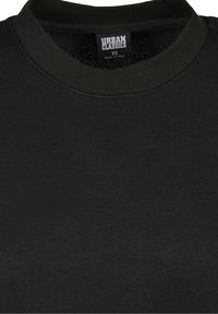 T-shirt noir Black Urban Classics XS avec col rond et étiquette visible indiquant la taille et l'origine.