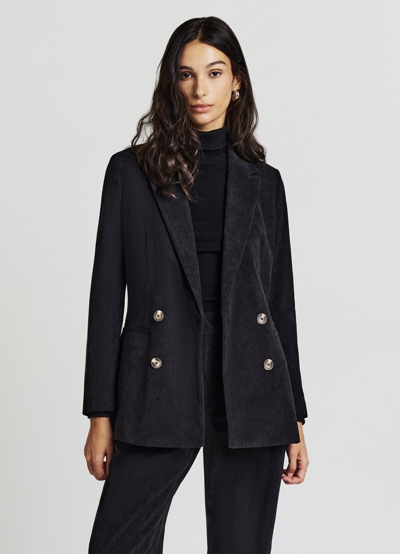 Blazer in velluto a coste nero con una vestibilità su misura, frontale doppiopetto, grandi bottoni dorati e rever sciallato. Tessuto morbido e testurizzato.