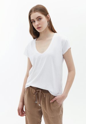 T-shirt bianca con scollo a V realizzata in tessuto leggero, con maniche corte e vestibilità ampia, abbinata a pantaloni marroni con cordoncino e tasche.