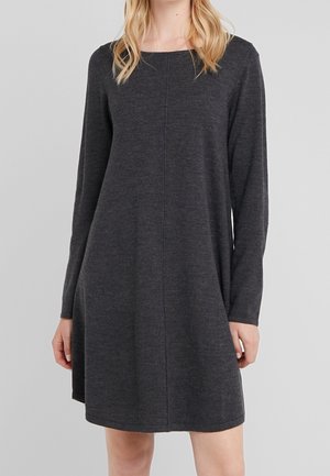 Femme portant une robe en maille gris foncé à manches longues avec un col rond, debout, les mains détendues le long du corps.