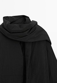 Sciarpa o avvolgente nera oversize in un tessuto testurizzato, caratterizzata da un design drappeggiato contemporaneo con morbide pieghe fluide e bordi.