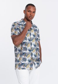 Chemise à manches courtes en tissu bleu clair avec un imprimé de feuilles tropicales dans des couleurs vertes, bleues et roses, offrant une coupe décontractée.