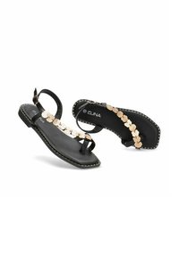 Sandalias planas negras con un acento metálico dorado, con un diseño de correa texturizada, hebilla en el tobillo y costuras blancas en contraste a lo largo de la suela.