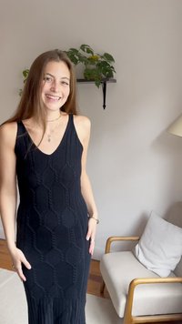 Juodas megztas suknelė su V formos iškirpte, turinti geometrinį raštą ir plisuotą dugną. Audinys atrodo minkštas su banguota tekstūra.