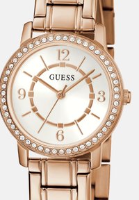 Roosa kuldne kell valge taustaga, kristallidega kaunistatud bezel ja linkmetallist rihm. Omab suuri tundemarke.