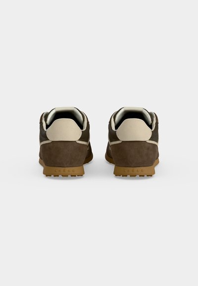 Paire de baskets décontractées marron et beige vues de dos sur un fond clair uni avec des semelles en caoutchouc et des colliers rembourrés.