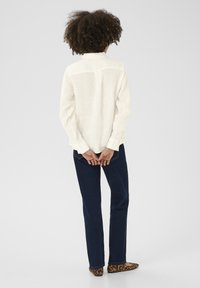 Light-colored linen shirt with long sleeves, blue jeans, and brown leopard print flats, viewed from the back. Plain background.