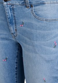 Gaiši zili džinsi ar rozā izšūtiem ziedu rakstiem, piecu kabatu dizains un kontrastējoša šuvju krāsa. Gluda tekstūra, klasiskā piegriezuma.