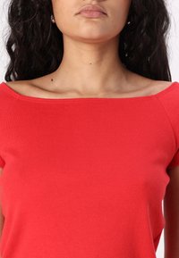 Červený, přiléhavý top bez ramínek vyrobený z hladké tkaniny, s jemnou texturou a krátkými rukávy, zvýrazňující čistý design výstřihu.