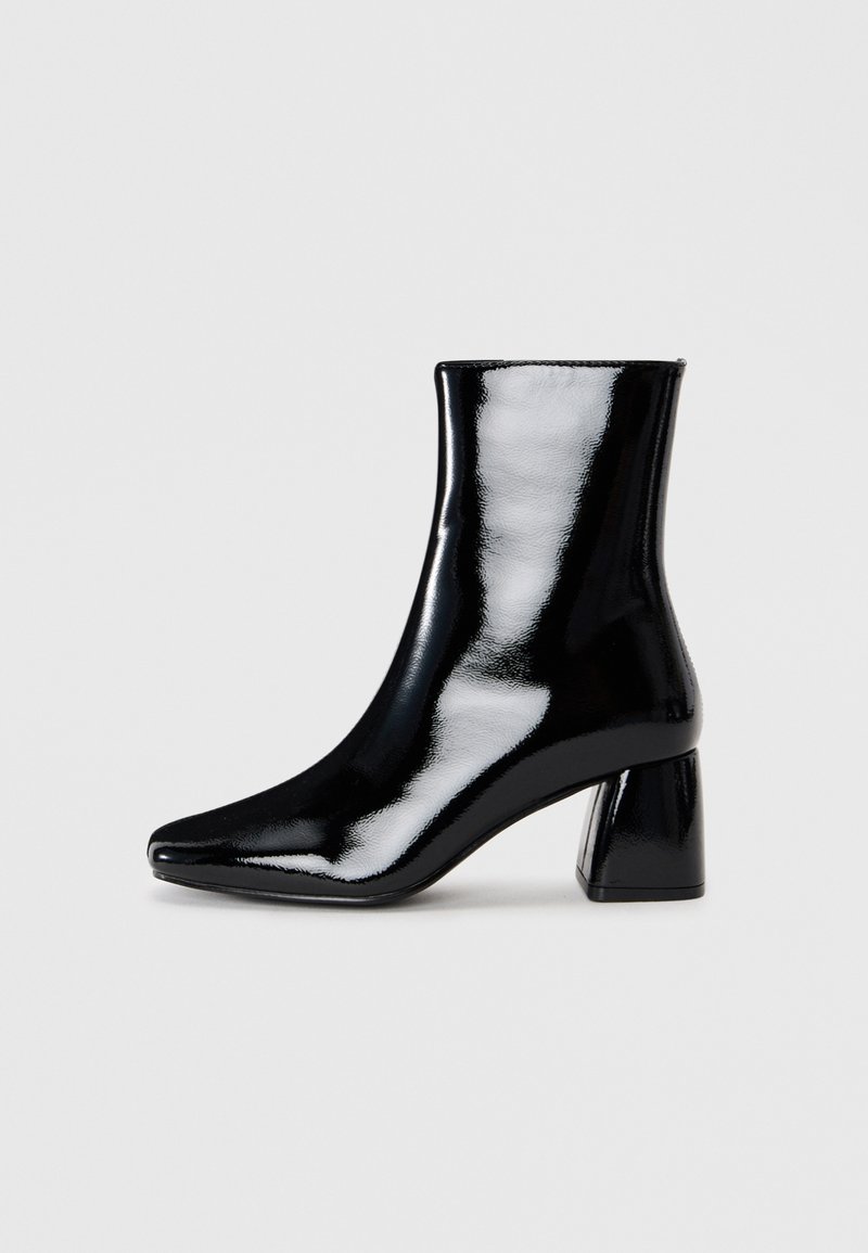 Schwarze Lack-Ankle-Boots mit einer spitzen Zehenpartie und einem quadratischen Blockabsatz. Glatte Textur mit hochglänzender Oberfläche, ohne sichtbare Verzierungen.