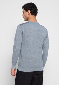 Lichtblauwe gebreide trui met een gestructureerd patroon, lange mouwen, ronde hals en contrasterende gestreepte accenten op de schouders.