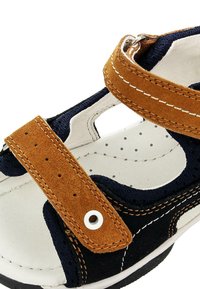Sandali in suede blu navy e beige con due cinturini regolabili, soletta perforata e impunture bianche a contrasto. Design aperto con dettagli in metallo circolari.